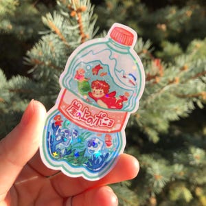 K&ouml;nnte beinhalten: Ein durchsichtiger Aufkleber f&uuml;r eine Plastikflasche mit glitzernder Oberfl&auml;che. Die Flasche ist mit blauer Fl&uuml;ssigkeit gef&uuml;llt und enth&auml;lt ein Cartoon-Bild eines rothaarigen M&auml;dchens in einem roten Kleid und einer Krone, umgeben von Fischen und Algen. Das Flaschenetikett lautet "海のポニー".