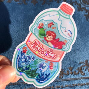 K&ouml;nnte beinhalten: Eine durchsichtige Plastikflasche mit rotem Verschluss, gef&uuml;llt mit Wasser und einem Comic-Charakter im Inneren. Die Flasche hat japanischen Text auf der Seite, der "海のボトル" lautet.