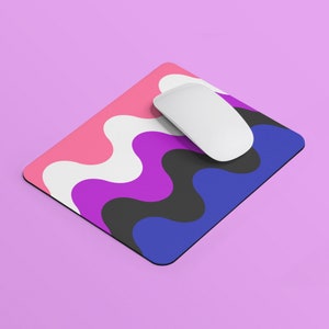 Puede incluir: Una alfombrilla de ratón colorida con un patrón ondulado en rosa, blanco, morado, negro y azul. Un ratón de ordenador blanco está encima de la alfombrilla de ratón.