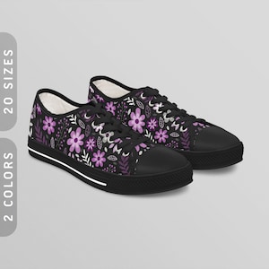 May include: A pair of black canvas shoes with a purple floral pattern. The shoes have white laces and a white stripe around the sole.