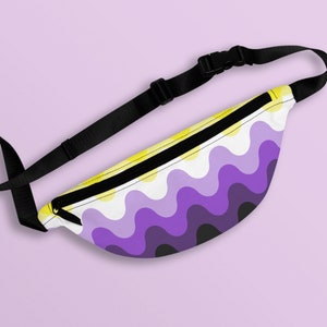 Pode incluir: Uma pochete com um design da bandeira do orgulho não binário. A bolsa apresenta um padrão ondulado em amarelo, branco, roxo e preto. Possui uma alça ajustável preta e um fecho de fivela preto. O fundo é lilás claro.