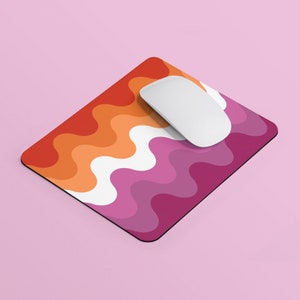 Puede incluir: Un ratón de ordenador blanco sobre una alfombrilla de ratón con un patrón ondulado en tonos naranja, rosa y blanco.