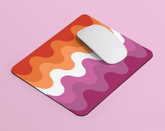 Puede incluir: Un ratón de ordenador blanco sobre una alfombrilla de ratón con un patrón ondulado en tonos naranja, rosa y blanco.