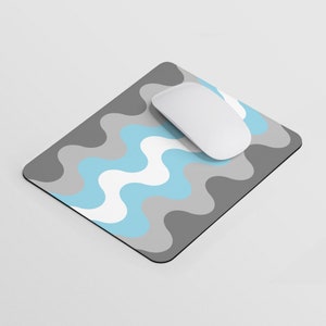 Puede incluir: Una alfombrilla de ratón con un patrón ondulado gris y azul con un ratón de ordenador blanco en la parte superior.