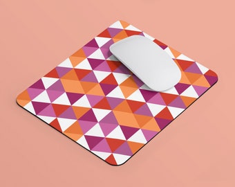 Puede incluir: Un ratón de ordenador blanco descansa sobre una alfombrilla de ratón con un patrón geométrico. La alfombrilla presenta un diseño repetido de triángulos en tonos naranja, rosa, rojo y blanco. La alfombrilla es rectangular con esquinas redondeadas.