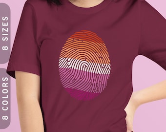 May include: A maroon t-shirt with a fingerprint design in the colors of the lesbian pride flag. The fingerprint is orange, white, pink, and purple.