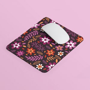 May include: A black mouse pad with a floral pattern featuring pink, orange, and white flowers on a dark background. A white computer mouse is on top of the mouse pad.