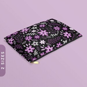Puede incluir: Una bolsa negra con cremallera con un estampado floral morado y blanco. La bolsa está hecha de tela y tiene una cremallera dorada.