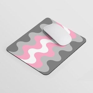 Puede incluir: Una alfombrilla de ratón con un patrón ondulado rosa, gris y blanco con un ratón de ordenador blanco en la parte superior.