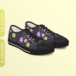 Peut inclure: Une paire de baskets basses en toile noire avec un imprimé floral composé de fleurs violettes, jaunes et blanches sur un fond gris foncé.