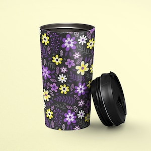 Puede incluir: Una taza de viaje negra con un patrón floral con flores moradas, amarillas y blancas sobre un fondo oscuro. La taza tiene una tapa negra con una tapa abatible.