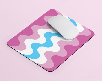 Puede incluir: Una alfombrilla de ratón con un patrón ondulado rosa y azul con un ratón de ordenador blanco en la parte superior.