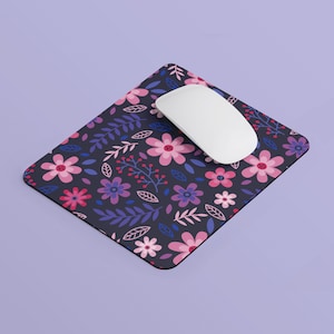 May include: A black mouse pad with a floral pattern featuring pink, purple, and blue flowers on a dark background. A white computer mouse is on top of the mouse pad.