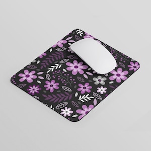 Peut inclure: Un tapis de souris noir avec un motif floral composé de fleurs et de feuilles violettes et blanches. Le tapis de souris est conçu pour être utilisé avec une souris d'ordinateur.