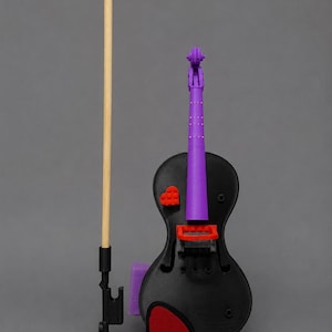 May include: A black violin with a purple neck and scroll, featuring a red heart-shaped brick on the body and a red chin rest. The instrument is accompanied by a bow consisting of a long wooden stick attached to a black plastic base.