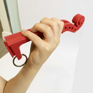 Könnte beinhalten: Ein roter, 3D-gedruckter Geigen-Schlüsselanhänger. Der Schlüsselanhänger hat eine Schnecke, ein Griffbrett und einen Schlüsselring. Das Design ahmt eine Miniaturgeige nach, mit Details wie Wirbelkasten und f-Löchern. Der Schlüsselanhänger wird in einer Hand gehalten.