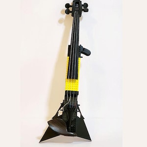 Puede incluir: Un violín eléctrico construido con bloques de construcción de plástico negro y amarillo. El instrumento cuenta con un diapasón negro, una mentonera negra, cuatro clavijas en el clavijero y un puente con cuerdas que recorren el cuerpo.