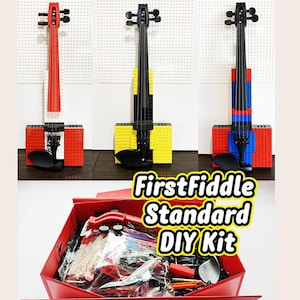 Puede incluir: Tres violines de juguete hechos con bloques de construcción coloridos. Uno es rojo, otro amarillo y el tercero azul. Los violines se muestran encima de una caja roja con la etiqueta "FirstFiddle Standard DIY Kit".