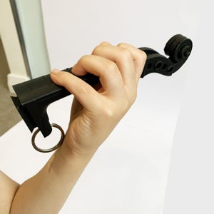 Könnte beinhalten: Ein schwarzer, 3D-gedruckter Geigen-Schlüsselanhänger. Der Schlüsselanhänger hat eine Schnecke, Wirbel und ein Griffbrett. Ein silberner Metallring ist an der Basis befestigt. Das Objekt wird vor einem weißen Hintergrund gehalten.