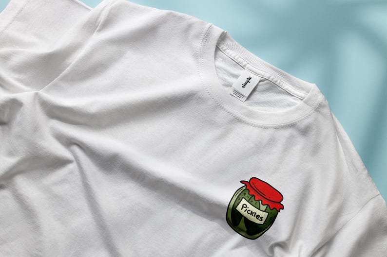 May include: White t-shirt with a cartoon illustration of a jar of pickles. The jar has a red lid and the label says "Pickles".