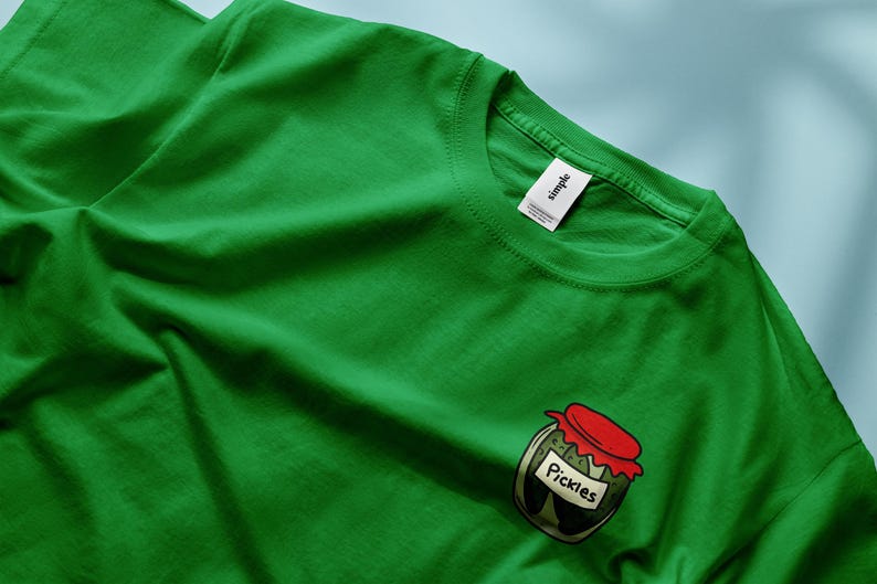 May include: A green t-shirt with a graphic of a jar of pickles. The jar has a red lid and the word "Pickles" is printed on the label.