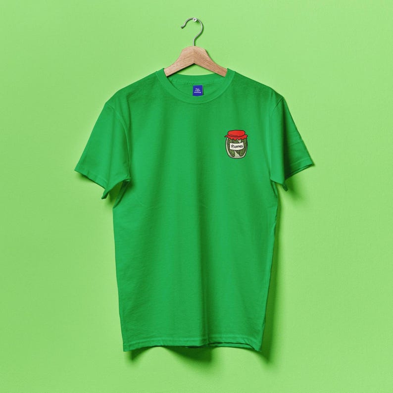 May include: A green t-shirt with a small embroidered image of a jar of pickles on the left chest. The jar has a red lid and the word "Pickles" is written on the label.
