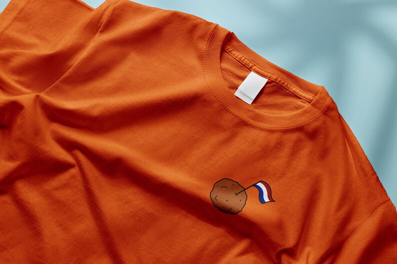 Może przedstawiać: Pomarańczowy T-shirt z małą brązowo-białą ilustracją holenderskiej flagi na mięsnej kulce.