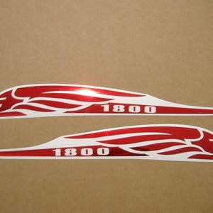Peut inclure: Deux autocollants rouges et blancs avec un motif de flamme stylisé et le numéro "1800" en blanc. Les autocollants sont allongés et incurvés, adaptés à une application sur un véhicule ou une surface similaire.