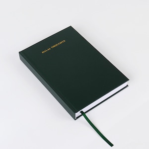 Pode incluir: Um diário de capa dura verde escuro com as palavras "HALAL THOUGHTS" impressas em dourado na capa. O diário tem um marcador de fita verde.