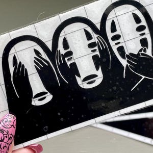 May include: Three black and white No Face stickers from the movie Spirited Away. The stickers are on a white grid background.