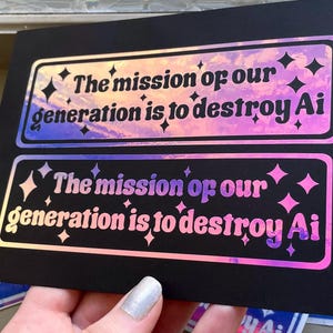 Puede incluir: Dos pegatinas rectangulares sobre una tarjeta negra, con texto holográfico que dice "The mission of our generation is to destroy Ai" rodeado de pequeñas estrellas. Las pegatinas tienen un acabado reflectante e iridiscente que cambia de color.