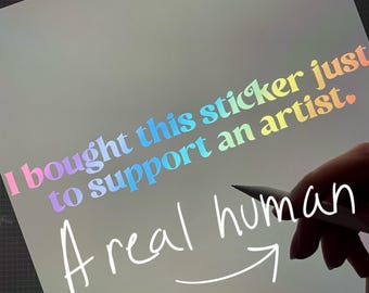 May include: A digital tablet screen displaying the text I bought this sticker just to support an artist. Below this, the handwritten text A real human with an arrow pointing to the right is visible. The interface shows various drawing tools.