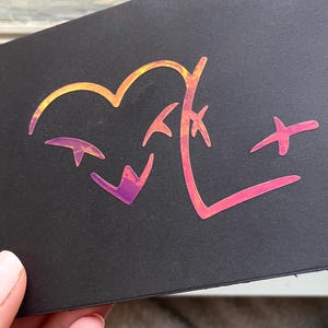 May include: Black card with a holographic design featuring a heart shape and abstract symbols in shades of orange, pink, and purple. The design is eye-catching and modern.