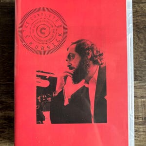 May include: A bright red DVD case featuring a black and white profile photograph of a bearded man. The text reads THE COMPLETE KUBRICK and THE CRITERION COLLECTION with the years 1951 and 1999 printed in a circular design at the top left.