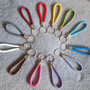 May include: A set of 12 colourful braided keychains with silver key rings. The keychains are in various colours, including red, yellow, green, blue, purple, white and brown.
