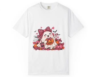 May include: A white short-sleeve t-shirt featuring a graphic of a cartoon ghost wearing a large pink leopard print bow. The ghost holds a small orange pumpkin and a pink drink cup, surrounded by smaller pumpkins, bats, and spiderwebs.