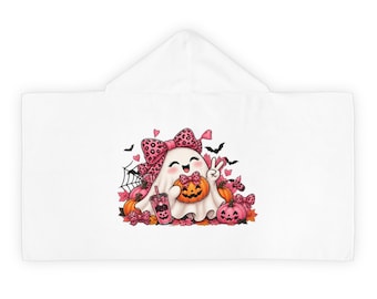 May include: A white hooded towel featuring a central graphic of a smiling ghost wearing a pink leopard print bow, holding a jack-o'-lantern and a pink drink. The design includes orange pumpkins, pink bows, small hearts, black bats, and a spider web.