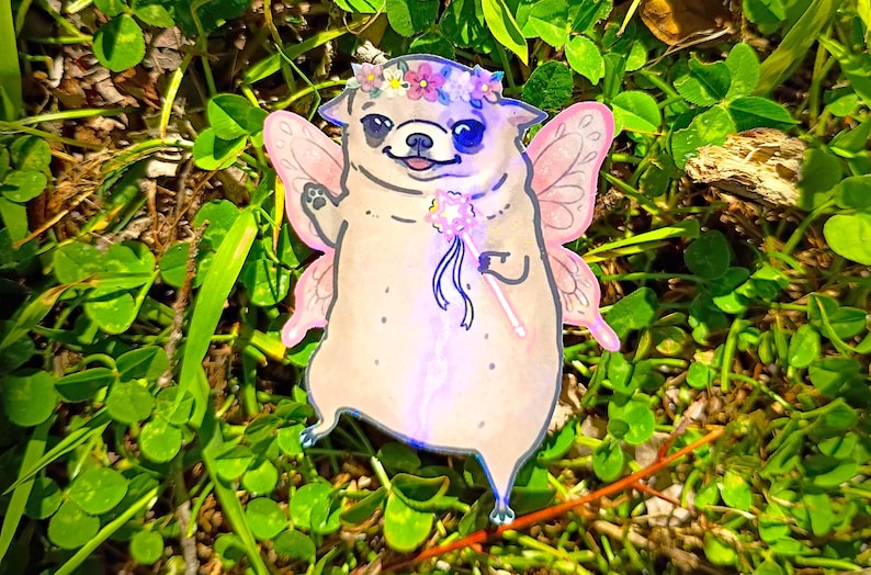 Pode incluir: Ilustra&ccedil;&atilde;o fantasiosa de um pug vestido de fada, completo com asas cor-de-rosa, uma coroa de flores e uma varinha m&aacute;gica. A obra de arte &eacute; ambientada em um fundo de grama verde e trevos.