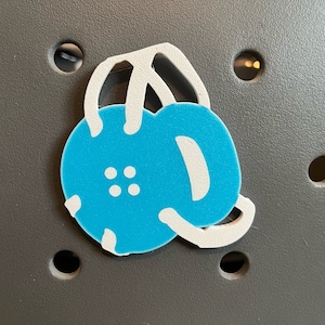 May include: A blue and white kettlebell sticker with a white outline. The sticker is on a gray surface.