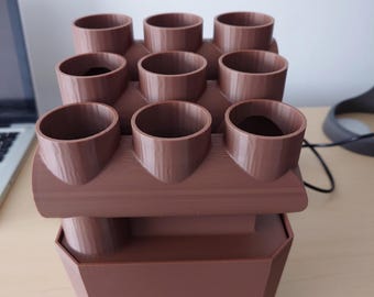 Peut inclure: Un pot de fleurs marron avec neuf ouvertures cylindriques disposées en trois rangées. Le pot a une base rectangulaire. Le design est moderne et fonctionnel, adapté aux petites plantes ou herbes. Le matériau semble solide et mat.