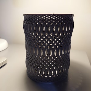 May include: A black, 3D printed, cylindrical container with a decorative, openwork design. The container has a textured, woven pattern with a geometric design.