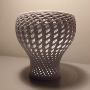May include: A white, 3D printed vase with a lattice design. The vase is shaped like a bell with a wide opening at the top and a narrow base.
