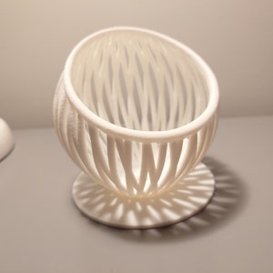 Può includere: Vaso da fiori in ceramica bianca a forma di uovo con un design a traliccio. Il vaso ha una base circolare.