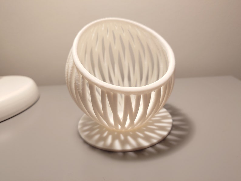 May include: White ceramic egg-shaped planter with a lattice design. The planter has a circular base.