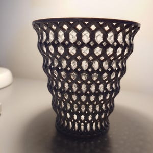 May include: A black, decorative vase with a geometric, lattice-like design. The vase is made of a translucent material, and the lattice pattern creates a unique visual effect.