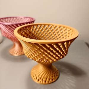 Può includere: Due ciotole decorative realizzate con un design a traliccio intrecciato. La ciotola a sinistra è rosa e la ciotola a destra è di colore marrone chiaro.