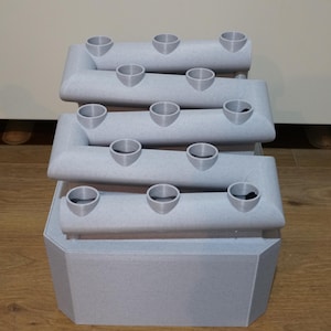 May include: A gray plastic tiered planter with multiple round holes for planting. The planter has a square base and is designed for vertical gardening.