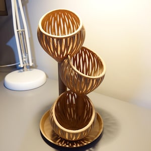 Könnte beinhalten: Ein dreistufiger Holzständer mit drei runden, geflochtenen Körben. Der Ständer ist aus Naturholz gefertigt und hat einen rustikalen, ländlichen Stil.