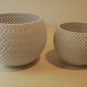 May include: Two white ceramic planters with a geometric pattern. The larger planter is in the foreground and the smaller planter is in the background.