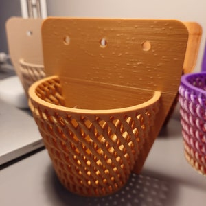 Puede incluir: Un conjunto de tres maceteros de pared hechos de plástico marrón. Los maceteros tienen un diseño de cesta tejida y tres agujeros en la parte posterior para colgar.